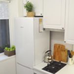 Белый холодильник у окна в маленькой кухне