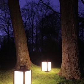 Переносные фонарики на траве между деревьями